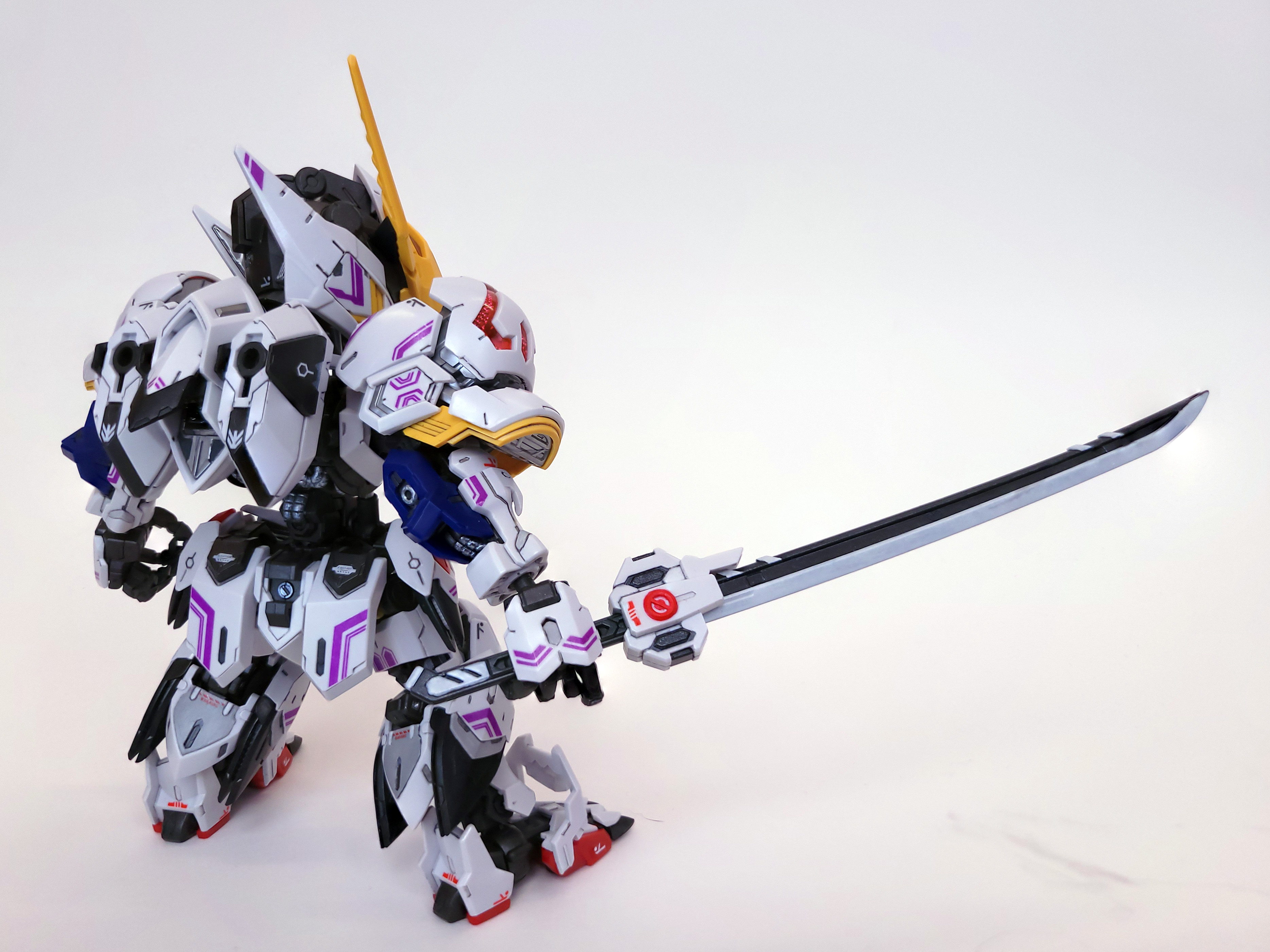 A white chibi gundam model with purple accents. It stands to the left of the frame, with its back to the camera, a white katana in its hand stretching into the whitespace of the right side of the frame.