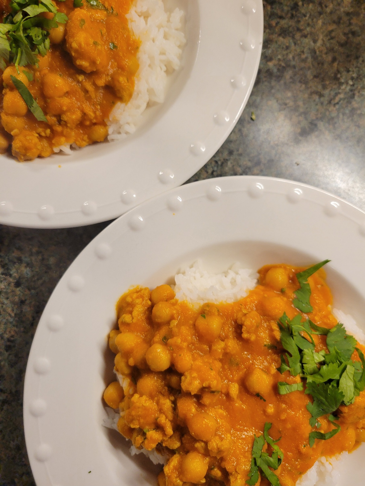 Two bowls of lovely orange curry on rice. The curry has chickpeas and ground sausage. Both are garnished with cilantro