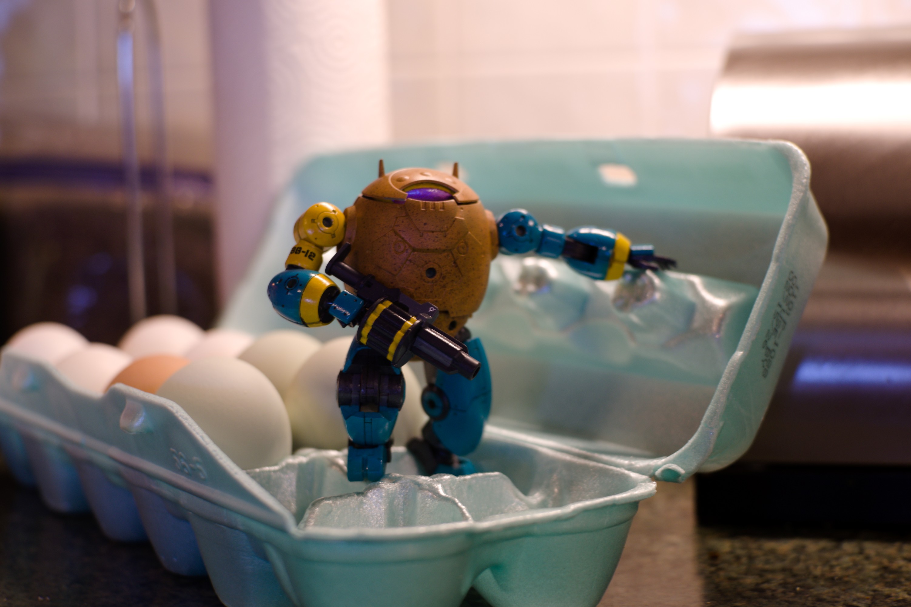 a robot shaped like a speckled brown egg with blue arms and legs stands nobly in an egg carton. It is carrying a grenade launcher and looking into the distance.