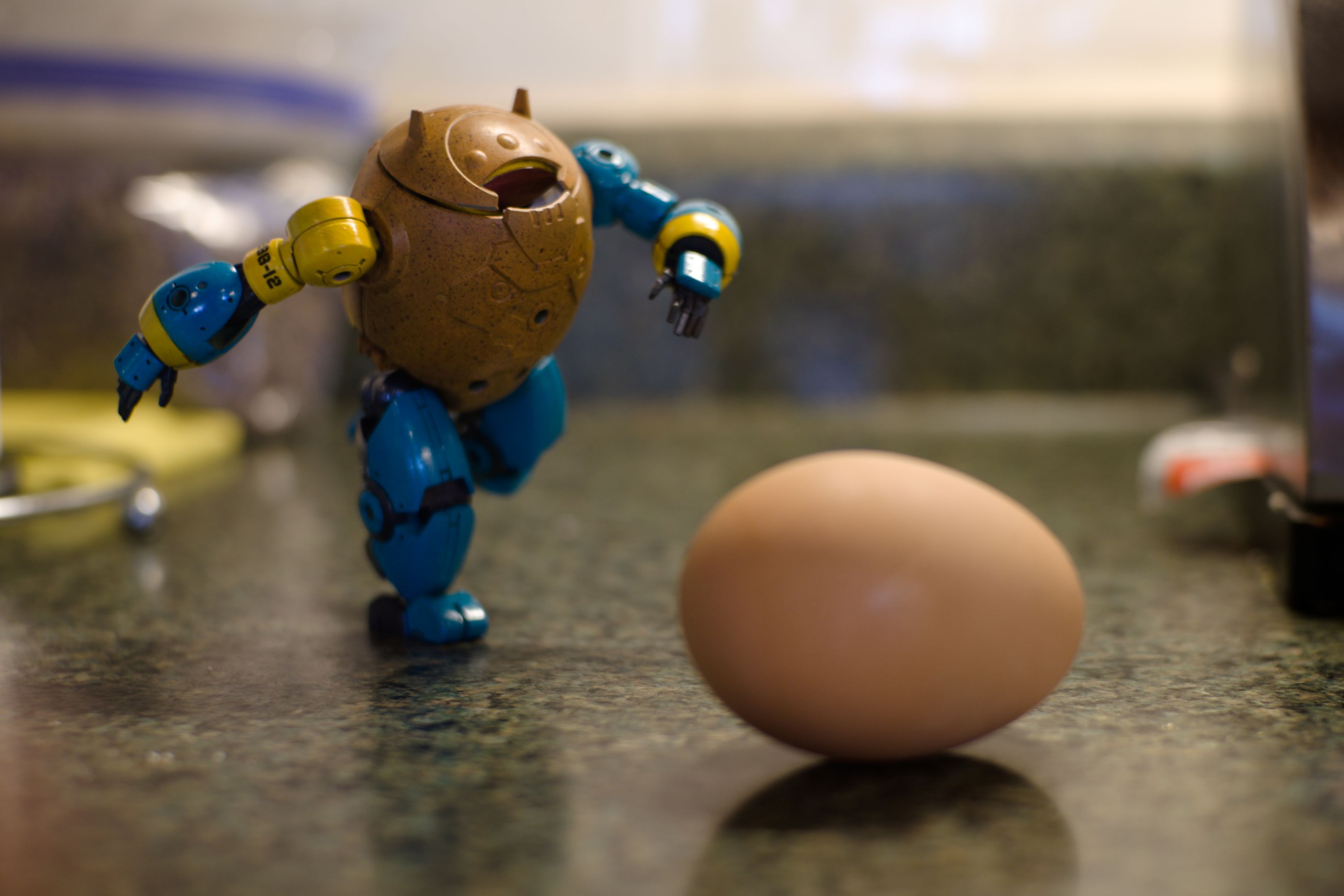 EGG-12 running toward a chicken egg resting on a kitchen counter. The egg and the robot's body are roughly the same size.
