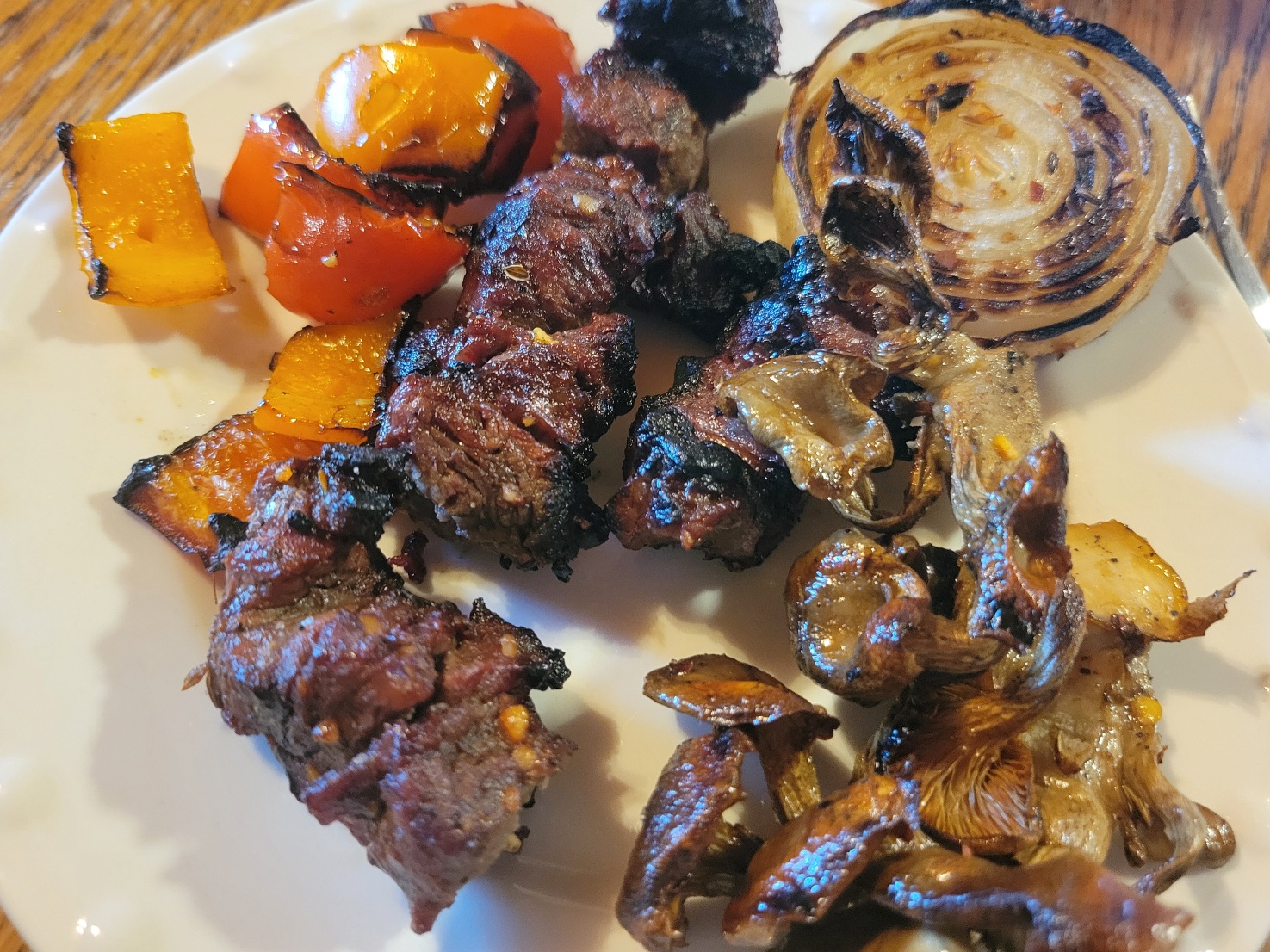 A plate of grilled chunks of steak, mushrooms, peppers, and onions all piled together