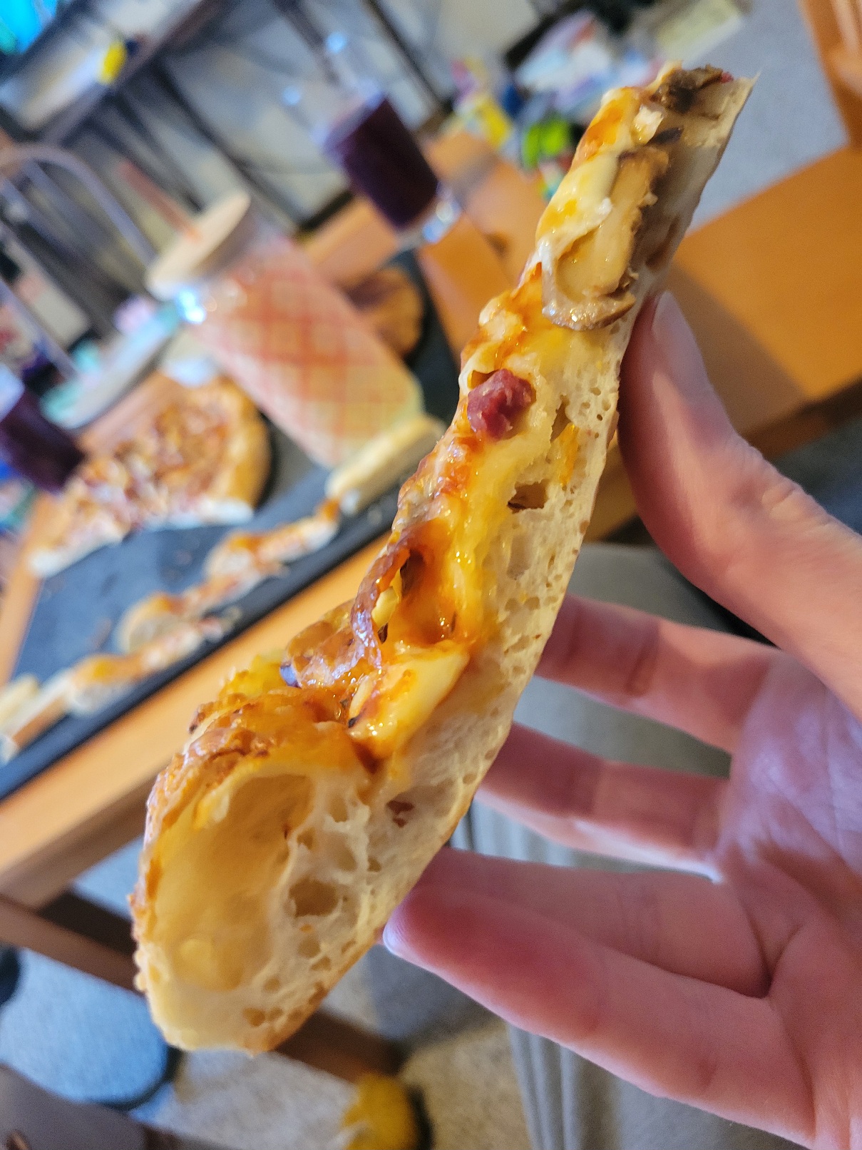 A slice of pizza seen from the side to show off the lofty crust's bubbles. A mushroom cheekily hangs off the crust near the point of the slice.