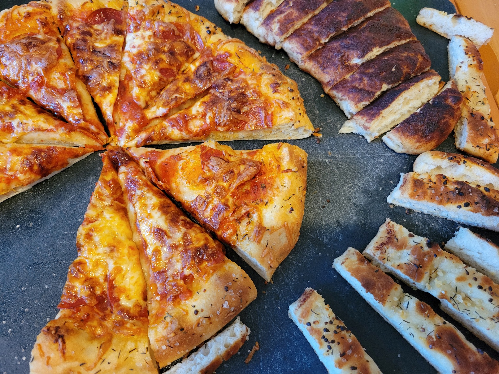 A pizza and two types of breadstick (cinnamon and garlic) arranged on a cutting board, several pieces removed.