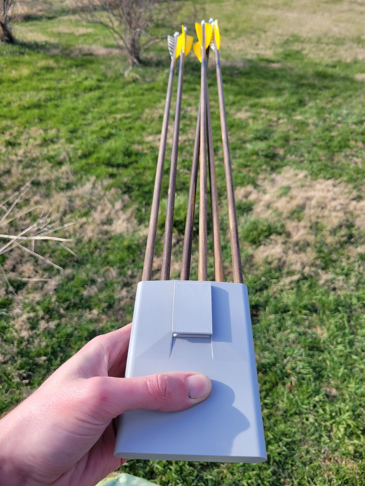a light grey 3D printed rectangle with a clip. There are six arrows extending out of it with yellow fletching
