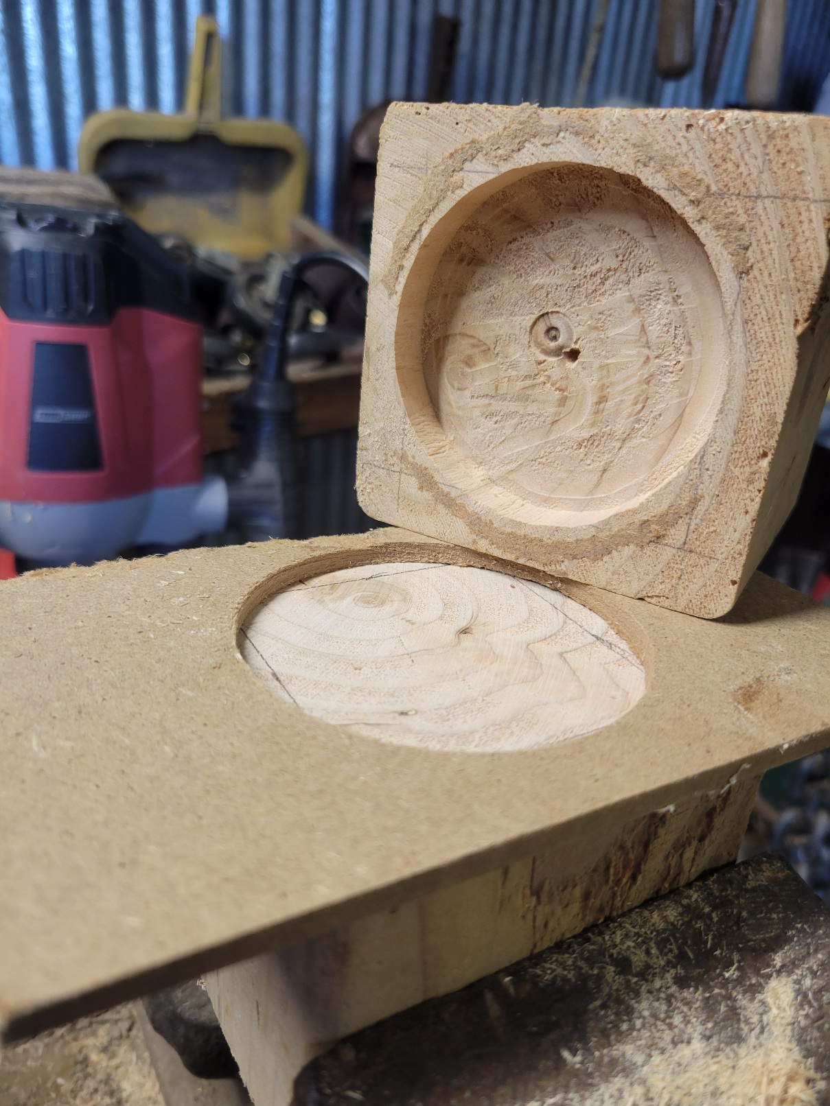 A block of wood is in a clamp, ready to be routed: a piece of MDF is glued onto it to guide the bit. Resting on this block is a second block, angled so its already complete routing cut can be compared with the clamped block