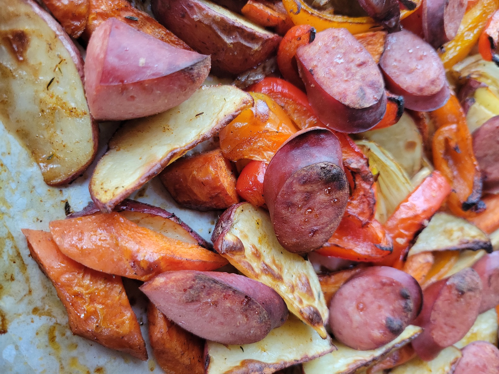 A closeup of a sheetpan crammed full of roast kielbasa, potatoes, carrots, onions, and peppers