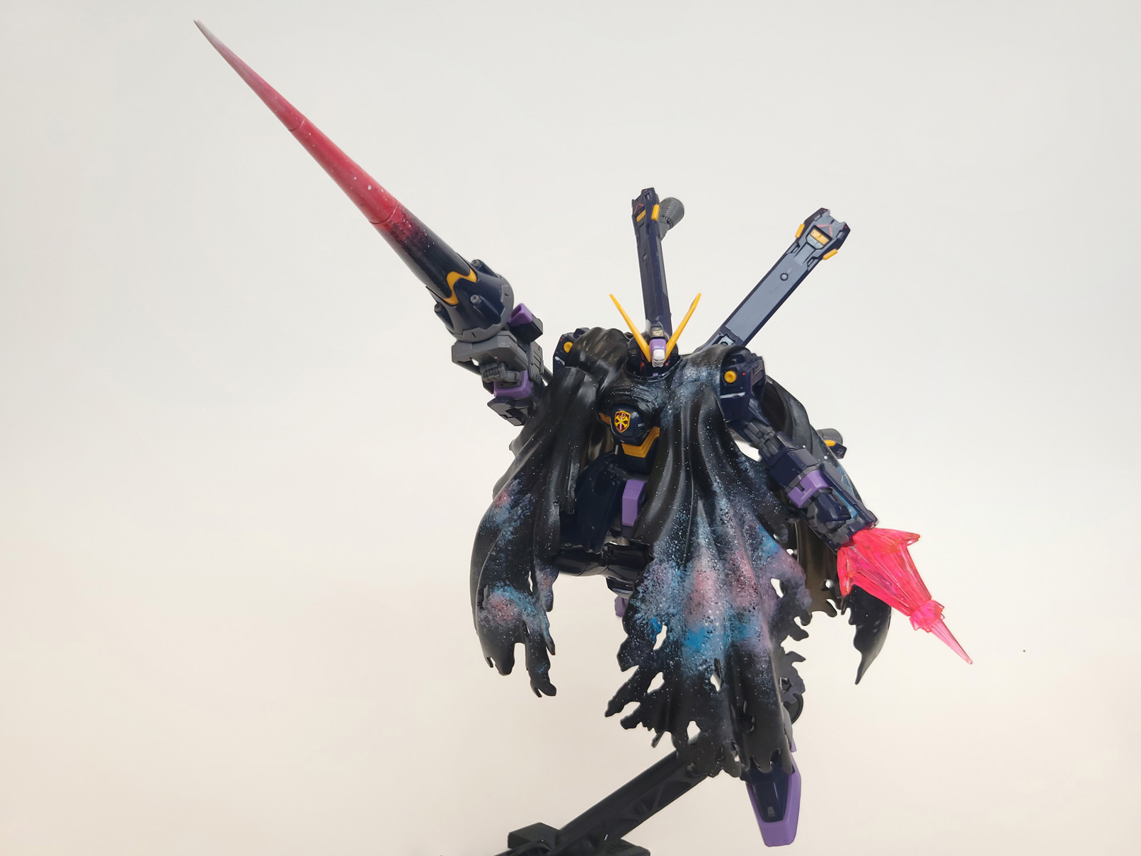 A navy blue robot shrouded in a cape painted with a nebula design. It carries a large lance with a gradient of white at the tip to pink to navy blue at the base.