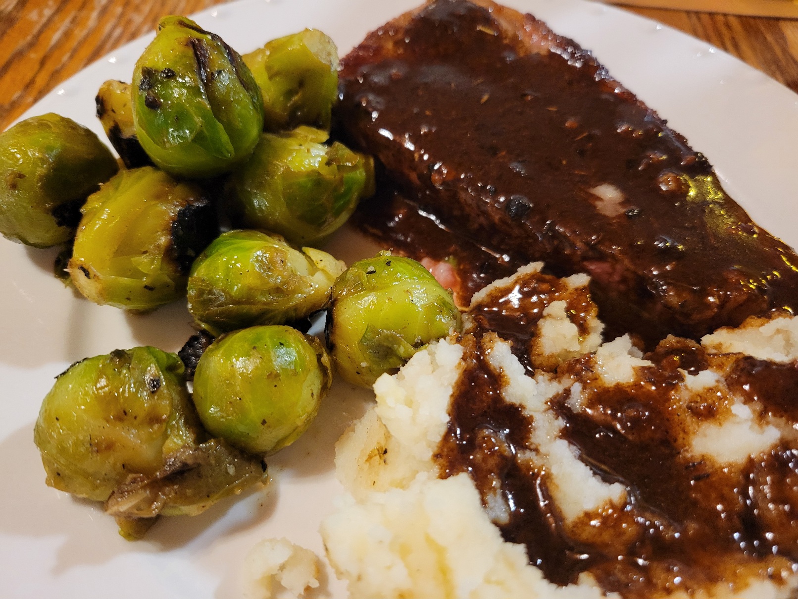 A plate of steak, mashed potatoes, and brussels sprouts. The steak and potatoes are coated in a dark brown pan sauce