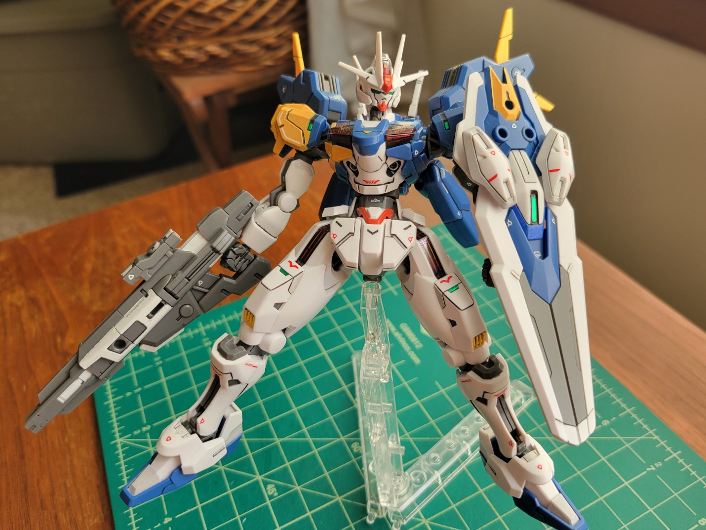 A blue, white, and yellow gundam model bearing a shield a laser gun. its stance is wide and strong