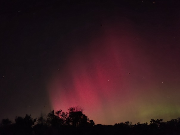 a long exposure photo of the night sky, there are waves of red shifting to green lighting the sky