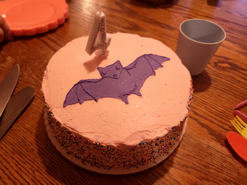 a pink birthday cake with sprinke-encrusted sides and a purple bat on top