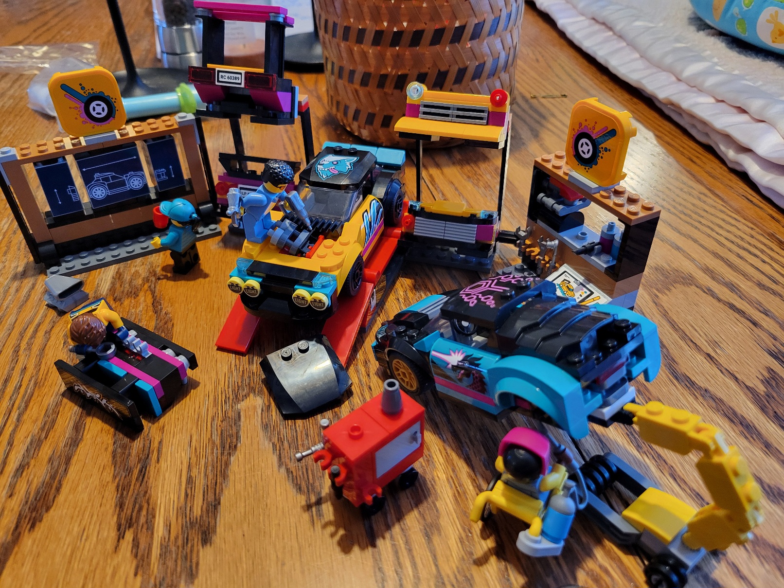 a lego car shop with two custom cars, four minifigs working on the cars, an abundance of tools, and several blueprints