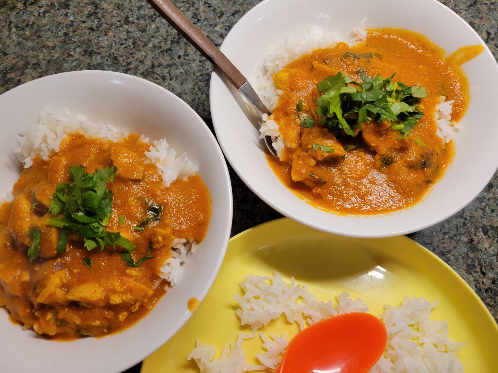 two bowls of curry garnished with cilantro next to a plastic plate of plain white rice