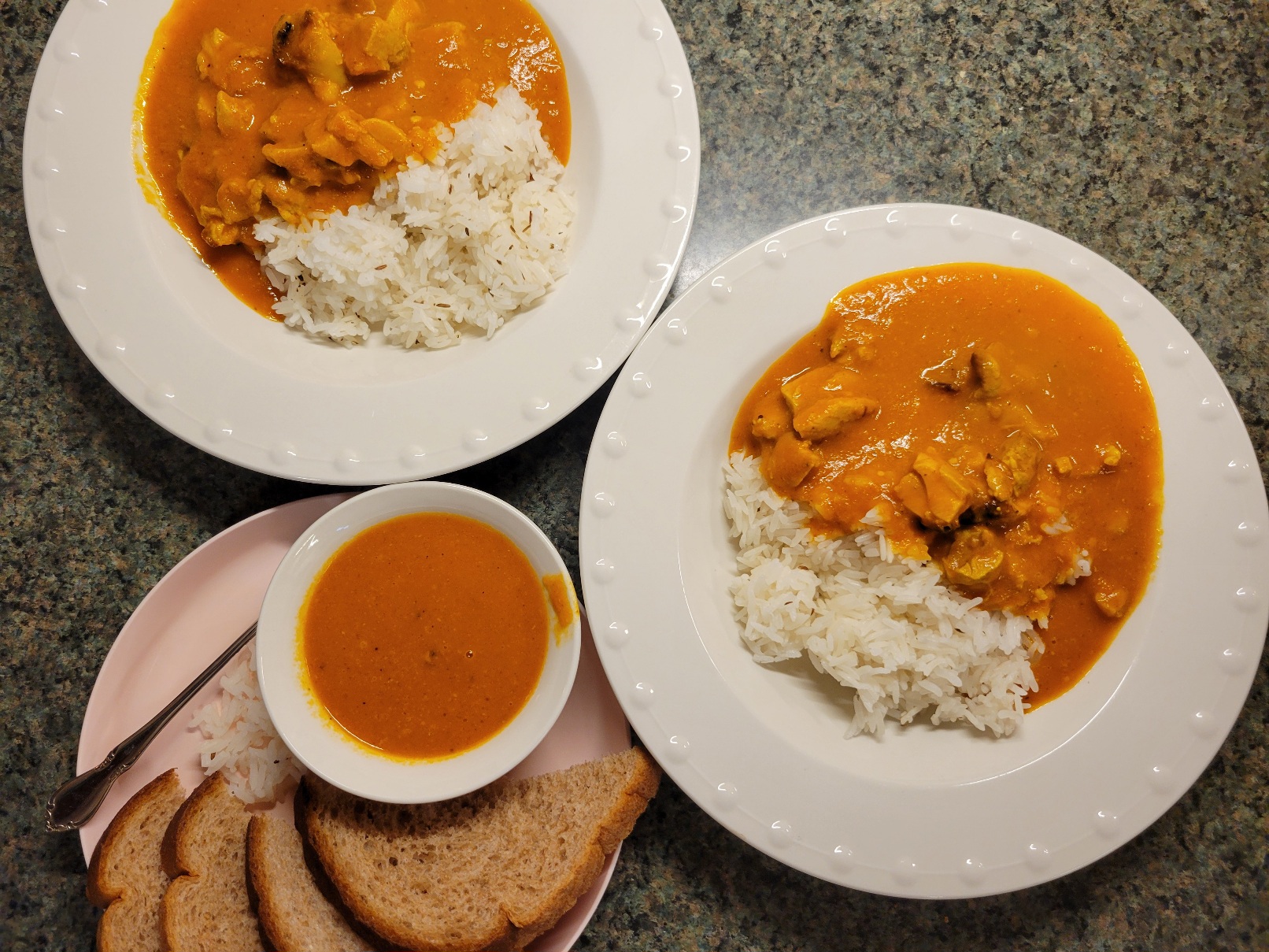 two bowls of curry plus a plastic plate with bread and a small bowl of curry sauce