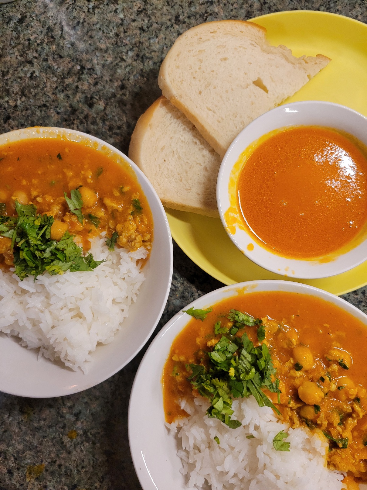 three bowls of curry, two large with rice and a sprinkling of cilantro, one small with bread instead of rice
