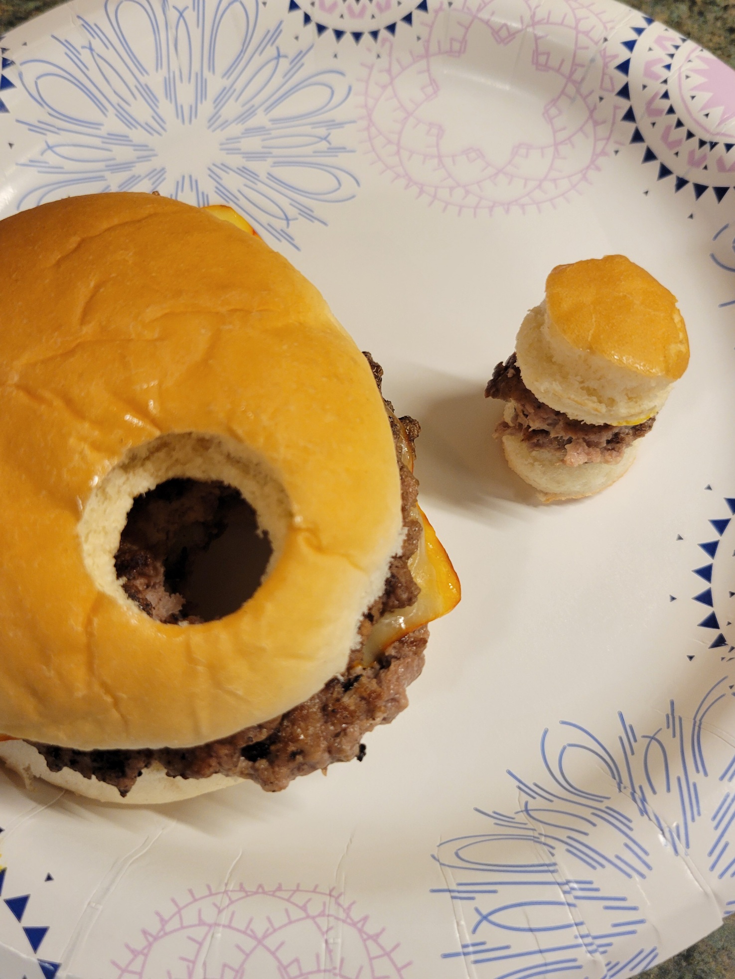 a tiny cheeseburger next to a full size one with a prominent and similarly sized hole through it