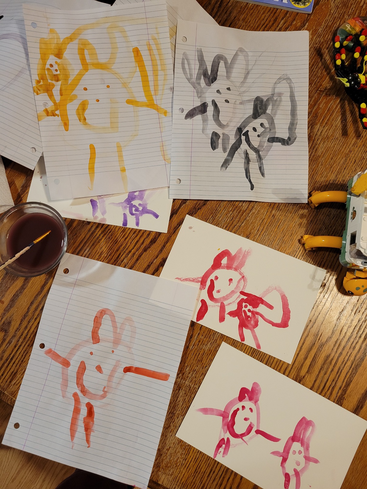 An assortment of paintings by a 5-year-old. Almost all of them feature two tadpole people side by side, one slightly smaller and both sporting bunny ears