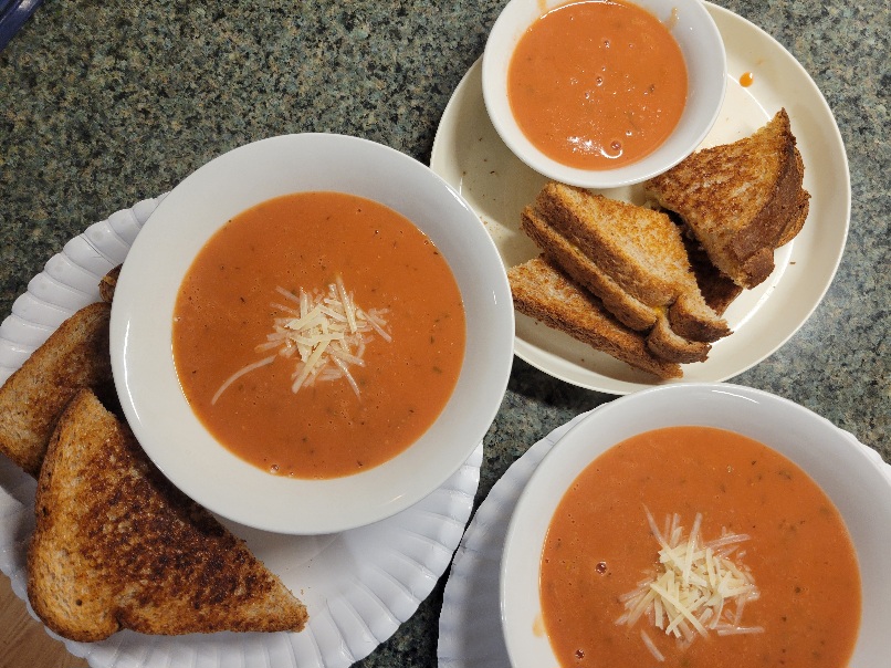 three plates and bowls of grilled cheese and tomato soup; one set is toddler-sized