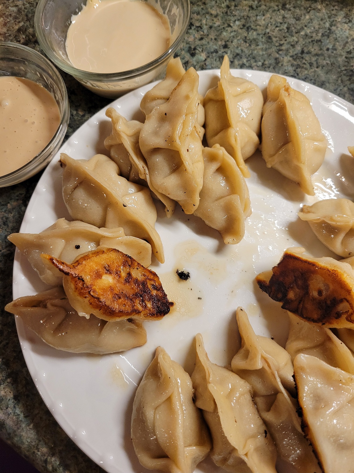 A plate full of pan-fried gyoaza. Two are flipped to show off their crispy bottoms