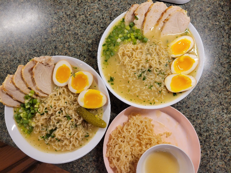 three bowls of ramen; two have marinated eggs and thinly sliced chicken, while the third is separated into noodles on a plate with a small bowl of broth