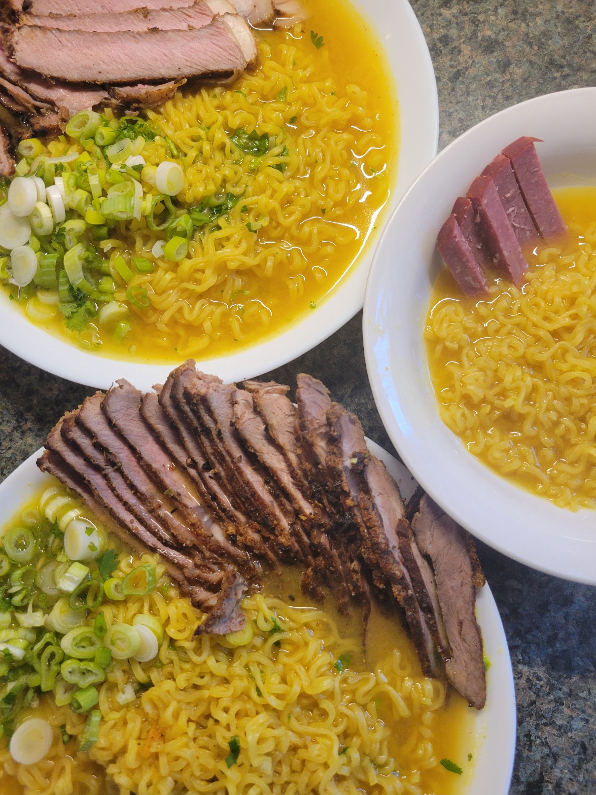 Three bowls of ramen; two large bowls with steakuand green onion, one small with smoked summer sausage