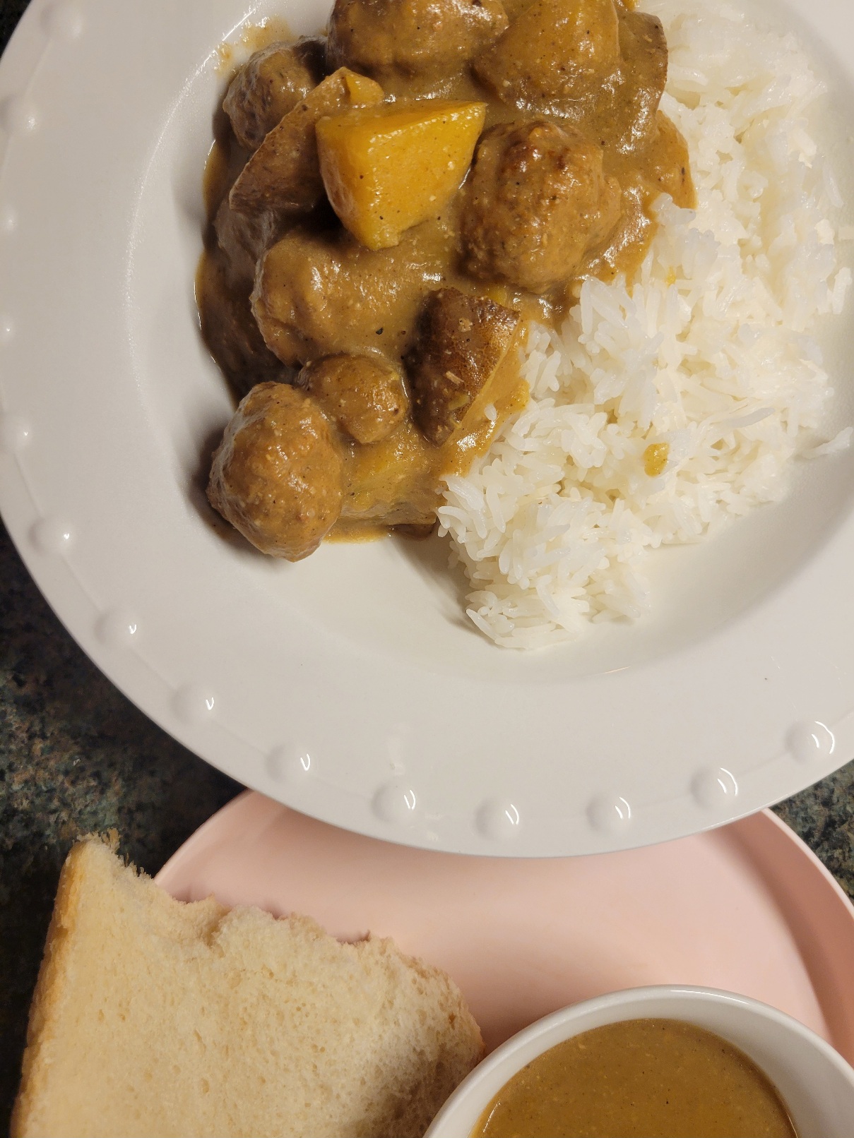 A bowl of golden korma with spicy lamb meatballs next to a small bowl of the korma gravy and bread