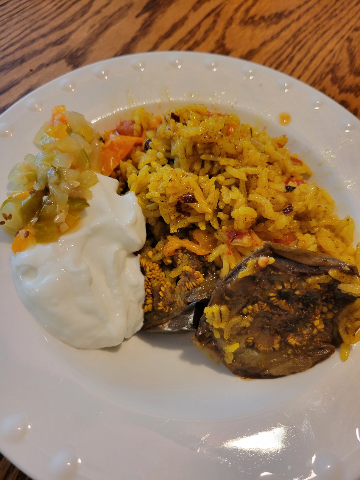 A bowl of maqloubeh with yoghurt, spicy butter drizzle, and dill relish