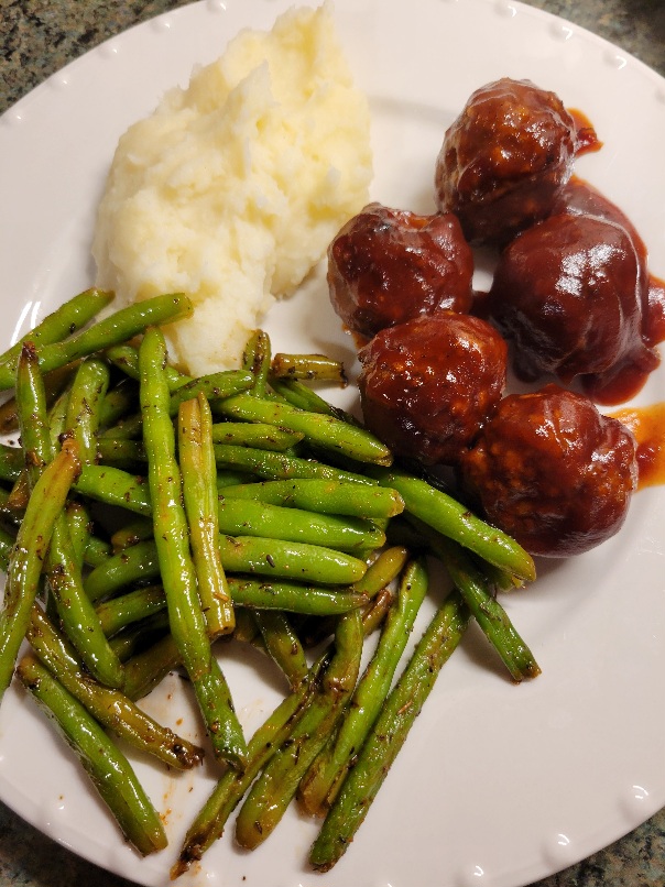 a plate of bbq meatballs, mashed potatoes, and green beans