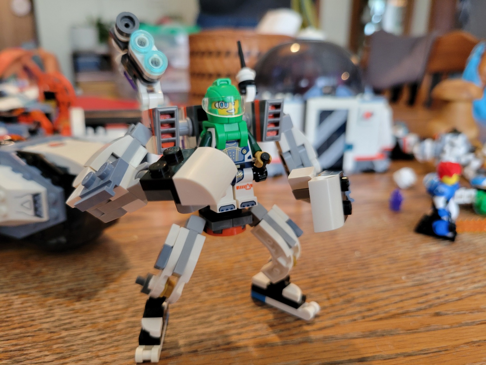 A white and grey lego mech with orange highlights. A lego astronaut in green pilots it via two levers