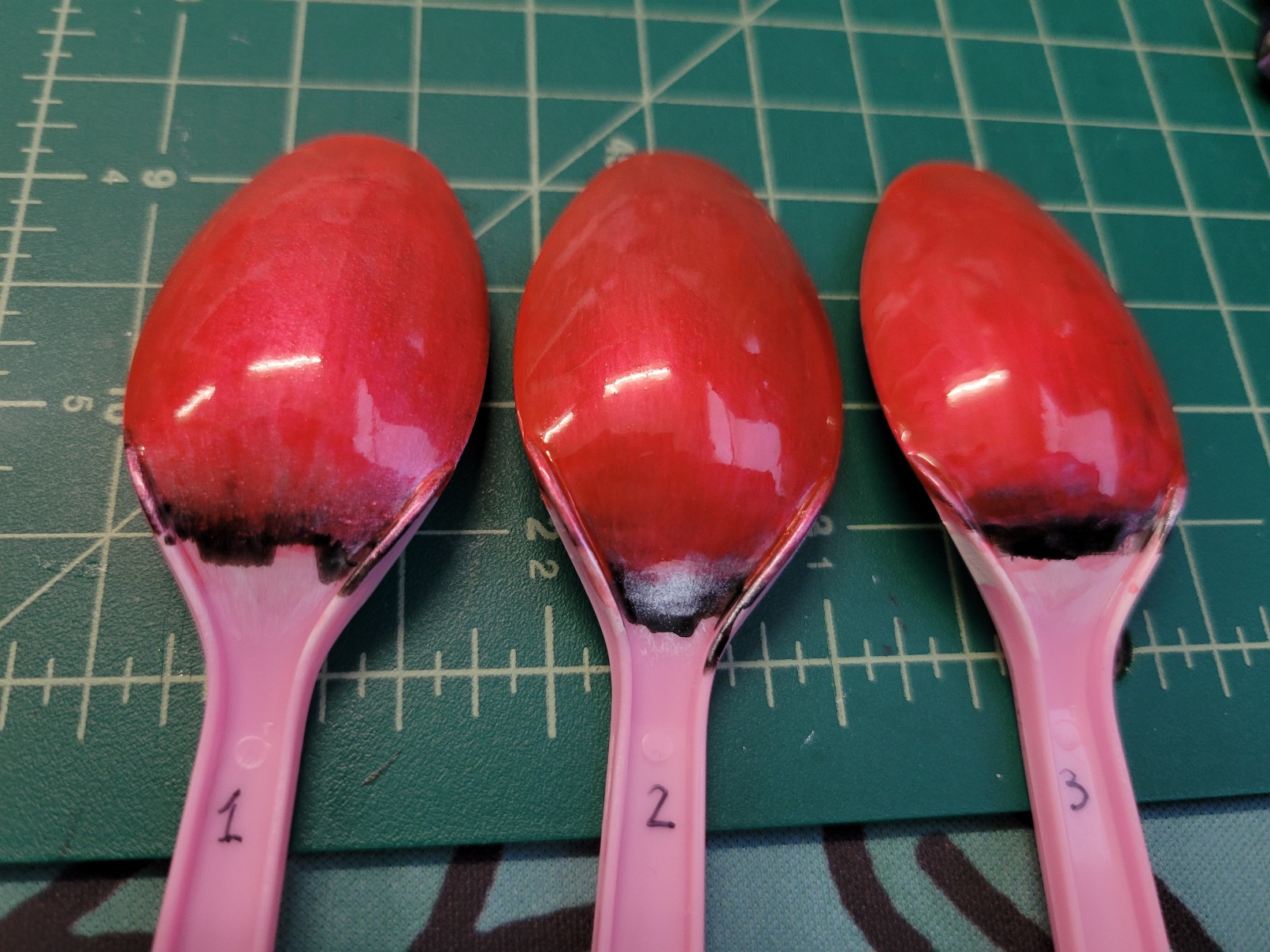 three plastic spoons in a line. The back side of each spoon bowl is painted a rich glossy red with a certain amount of depth
