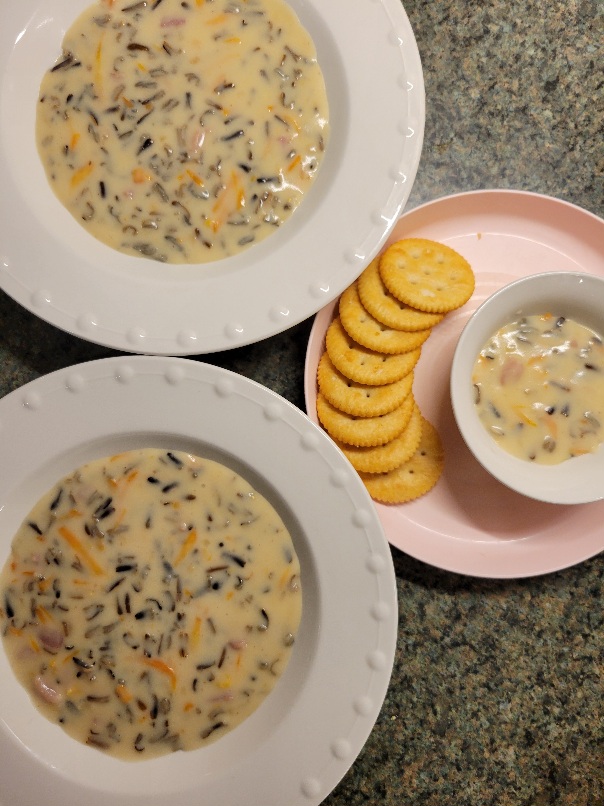 Two large bowls and one small bowl on a plate with crackers, all filled with wild rice soup