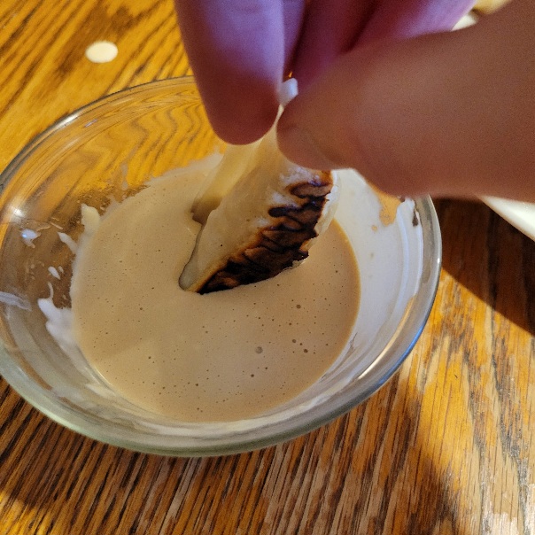 a potsticker dipped into a glass bowl of a light brown sauce