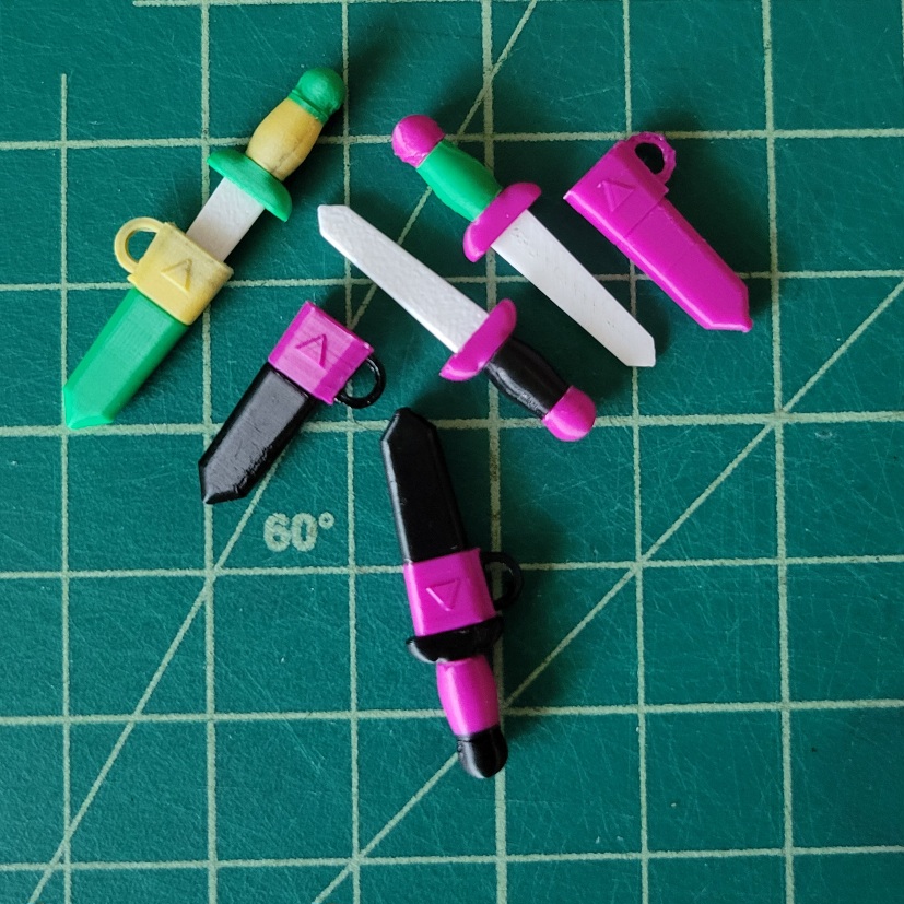 several very small brightly colored 3D printed swords, each about 3cm long. Some are inside of their sheaths, while others are outside, blades bare